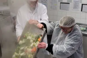 Deux personnes préparant une soupe aux légumes dans une cuisine.